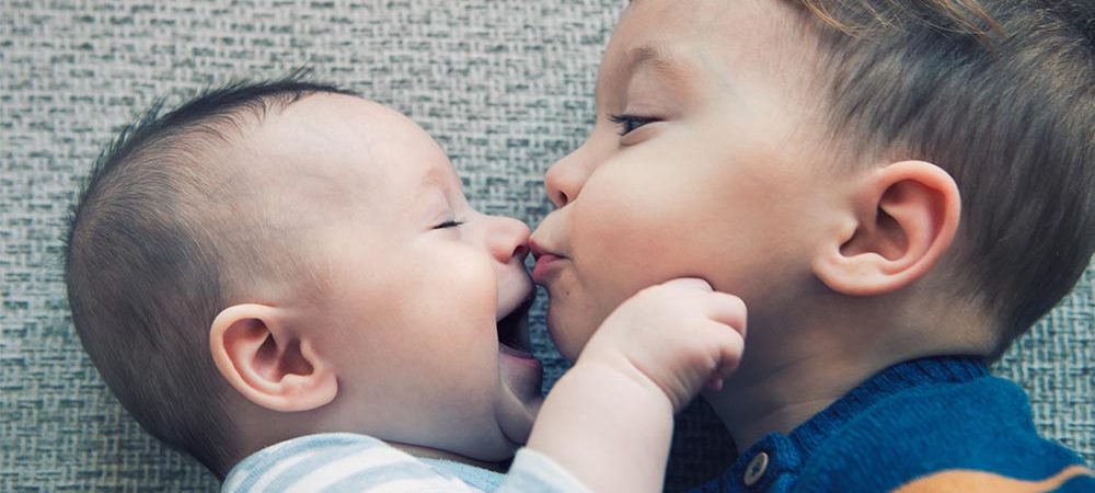 A toddler kissing a baby, two under two