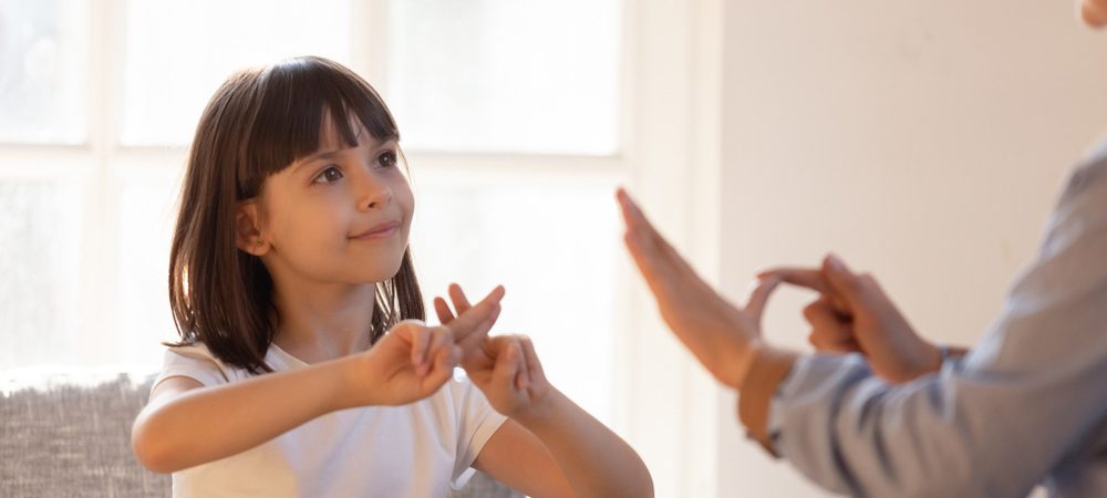 A young girl using sign language with an adult