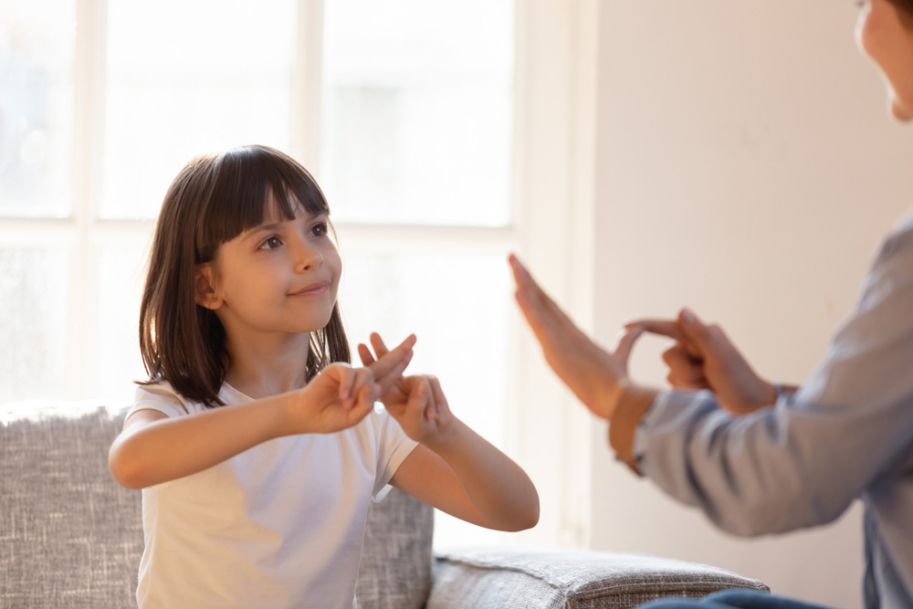 A young girl using sign language with an adult.