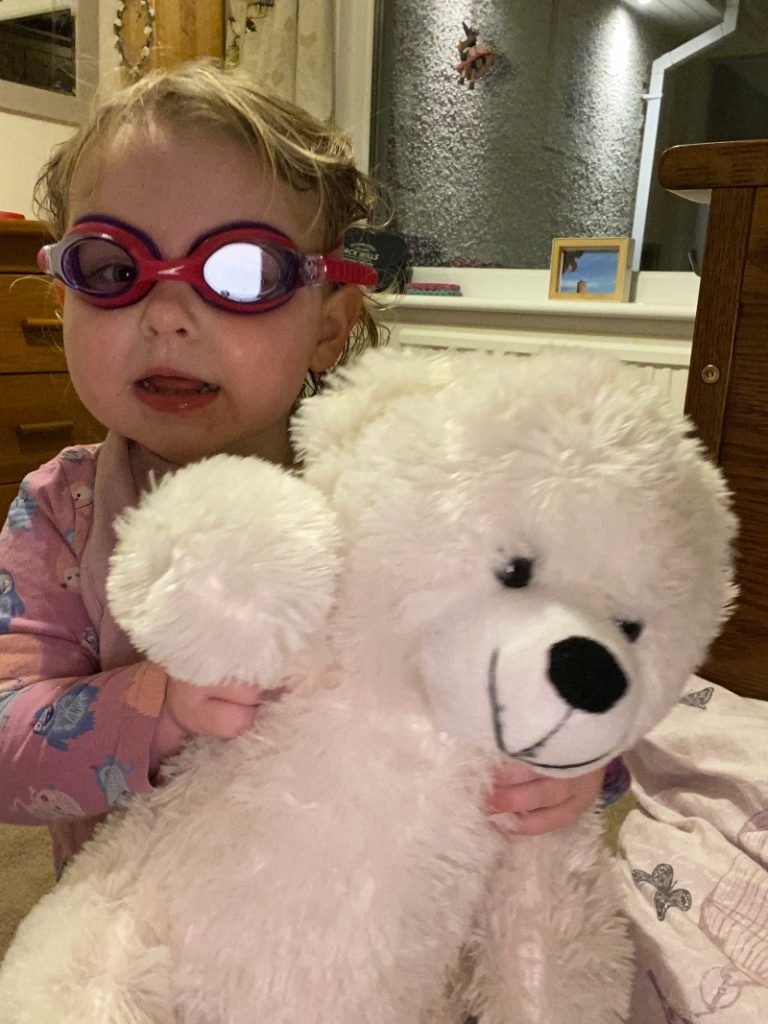 Milie holding snowy the bear dressed up with goggles and a tutu